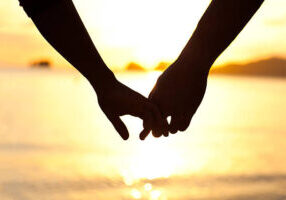 A couple holds hands on a beach at sunset.